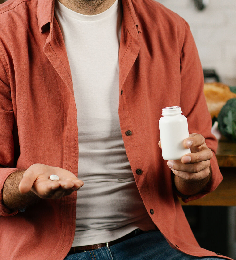 Homme tenant une pilule et un flacon de compléments alimentaires dans un cadre domestique