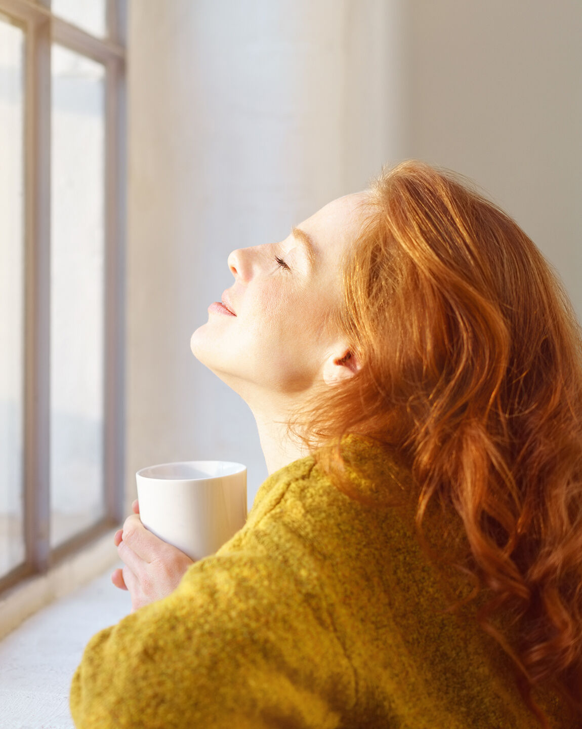 Femme rousse savourant un moment de détente au soleil, une tasse de thé à la main.