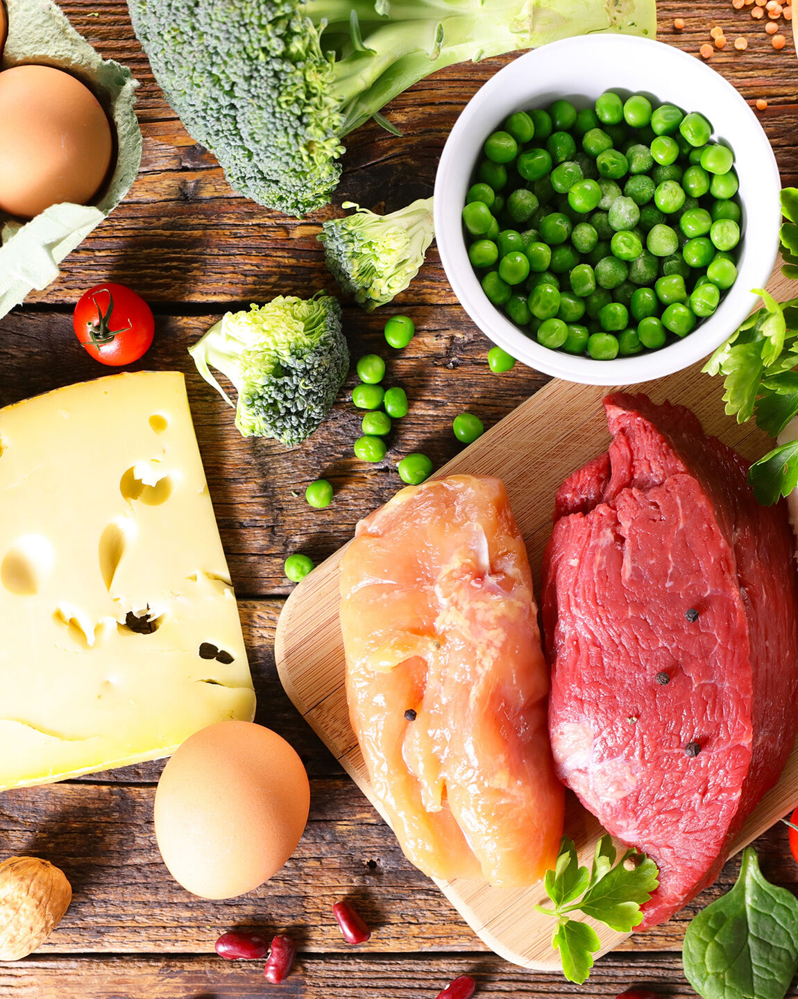Protéines animales et végétales : œufs, fromage, poulet, bœuf, brocolis, et pois verts sur une table en bois