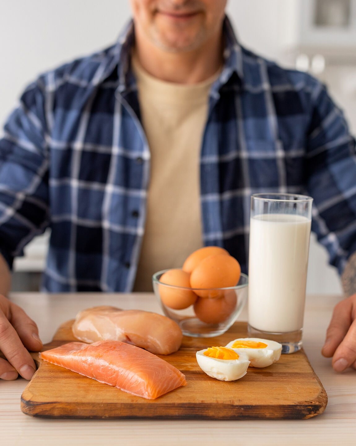 Un homme présentant des sources de protéines animales : saumon, poulet, œufs et verre de lait.