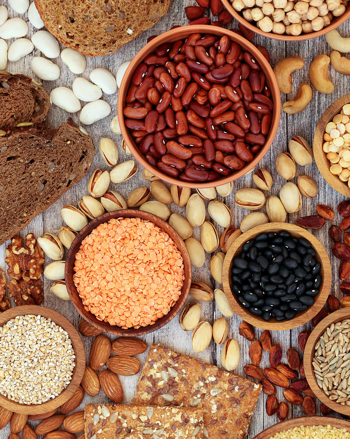 Sources de protéines végétales : lentilles, haricots rouges, pois chiches, noix, graines, et céréales complètesales et végétales : œufs, fromage, poulet, bœuf, brocolis, et pois verts sur une table en bois