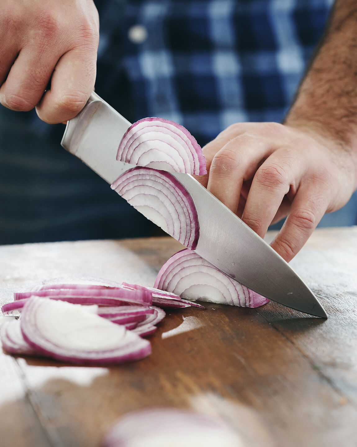 Main découpe des oignons rouges avec un couteau sur un plan de travail en cuisine