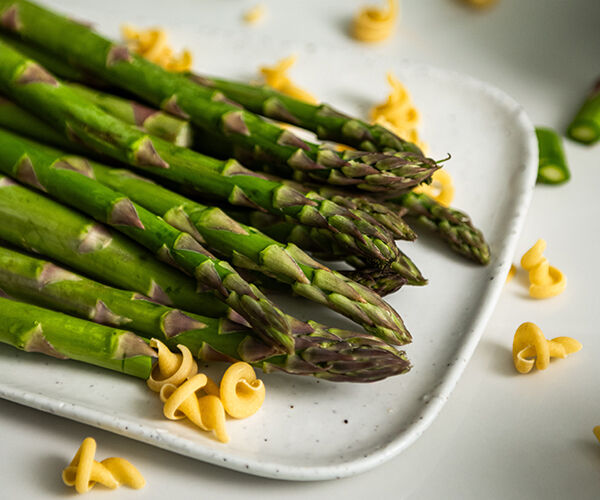 Présentation d'asperges vertes dans un plat avec quelques pâtes éparpillées en décoration