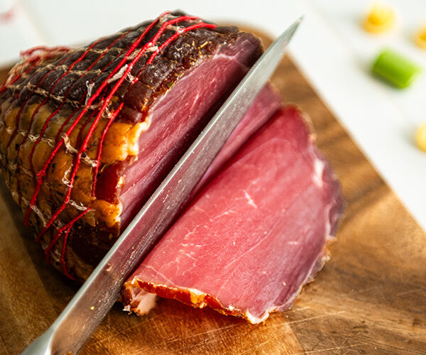 Découpe d'une noix de jambon d'Ardenne avec un couteau de cuisine sur une planche en bois