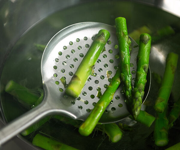 asperges coupées déposées avec une cuillère dans une poêle