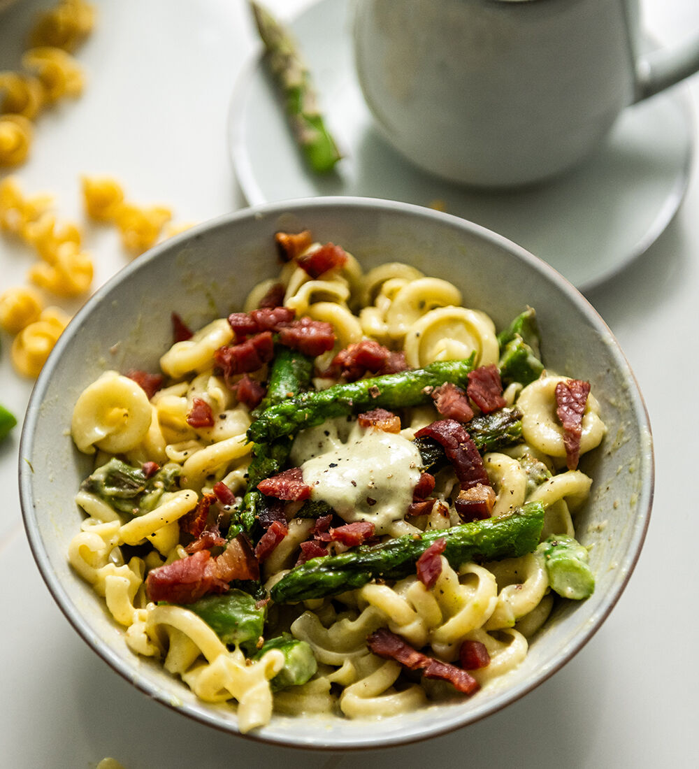 Plat final de la recette de Pâtes, asperges et jambon d'Ardenne accompagné de son pot de sauce. quelques ingrédients sont en décoration