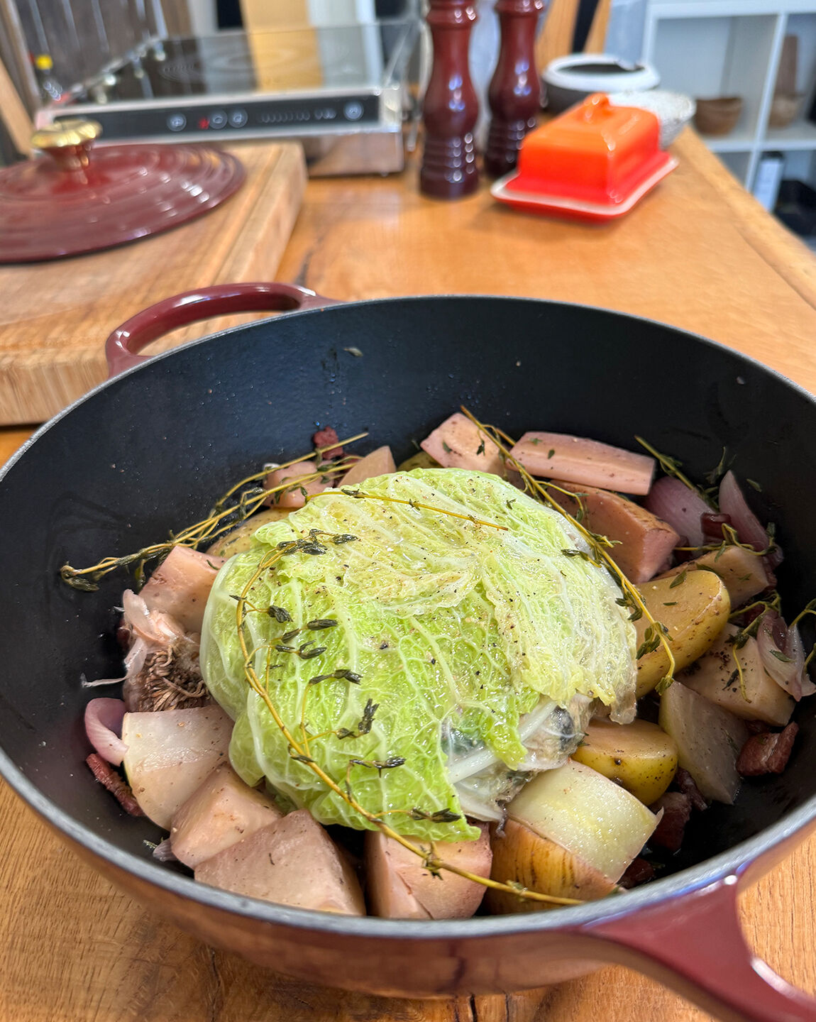 chou farci mijoté dans une cocotte en fonte, accompagné de légumes d’hiver et garni de branches de thym