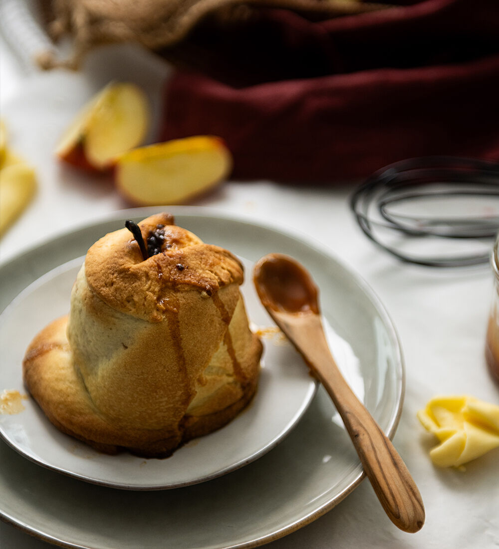 Douillon de pomme doré et croustillant, accompagné d’une cuillère en bois et de quartiers de pomme sur une table lumineuse
