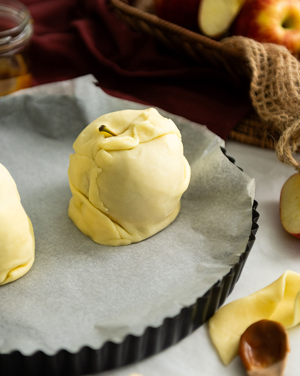 Douillon de pomme en préparation, une pomme enveloppée de pâte sur une plaque de cuisson recouverte de papier sulfurisé