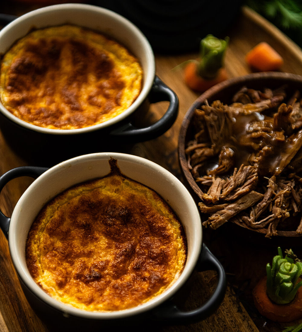 Soufflé de carottes doré et effiloché de bœuf avec sauce, présenté dans des ramequins noirs sur une table rustique