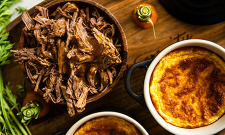 Plat de soufflé de carottes doré servi avec un bol d’effiloché de bœuf en sauce sur une planche en bois