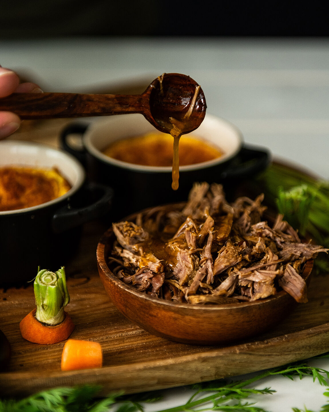 Effiloché de bœuf avec sauce versée à la cuillère, servi dans un bol en bois avec des soufflés de carottes en arrière-plan